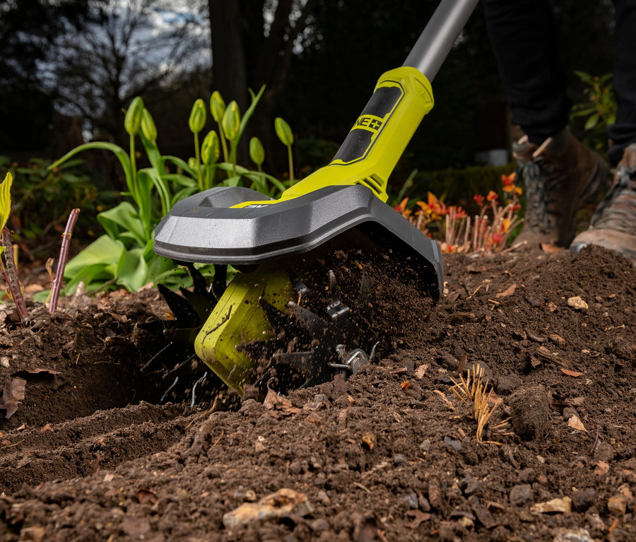 Eine Person benutzt eine RYOBI 18 V Akku-Bodenhacke »RY18CVA-0« um den Boden im Garten aufzulockern.