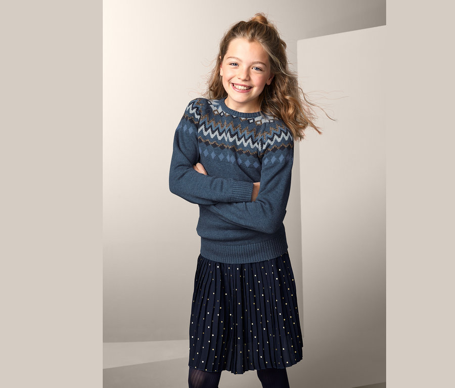 Mädchen posiert mit verschränkten Armen im Norweger-Strickpullover.