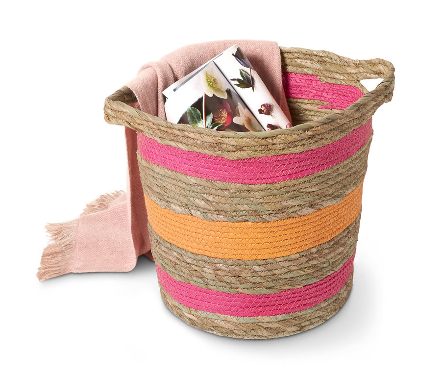 Ein Deko-Korb mit rosa und orangen Streifen, darin eine rosa Decke und eine Zeitschrift.