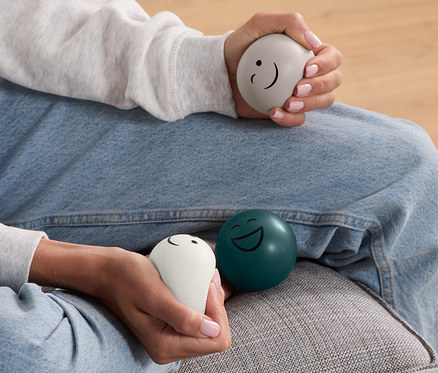Frau sitzt auf Couch und hält 3 Antistress-Bälle in den Händen.