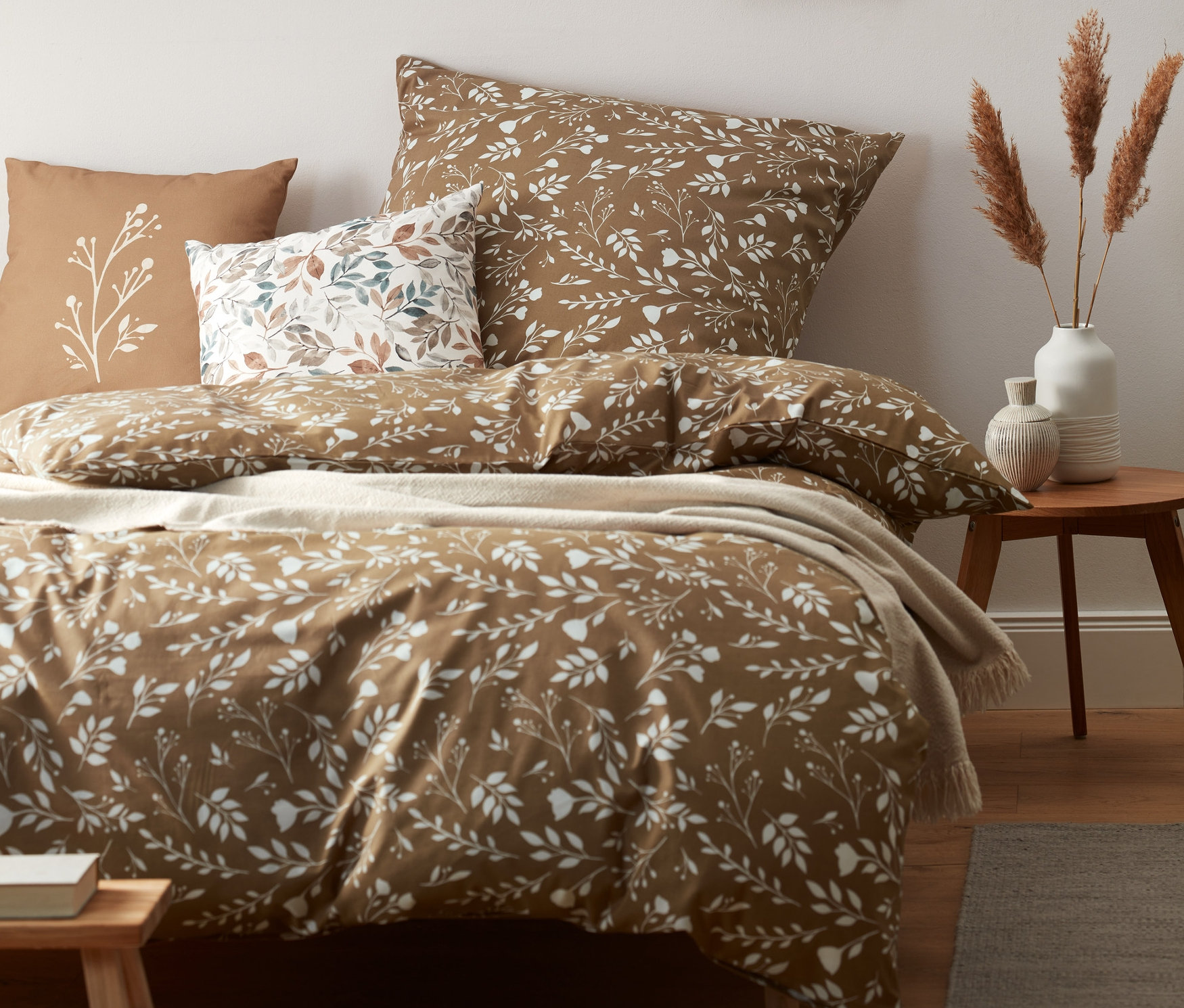 Ein braunes Bett mit weißer Blumenbettwäsche und braunen Kissen.