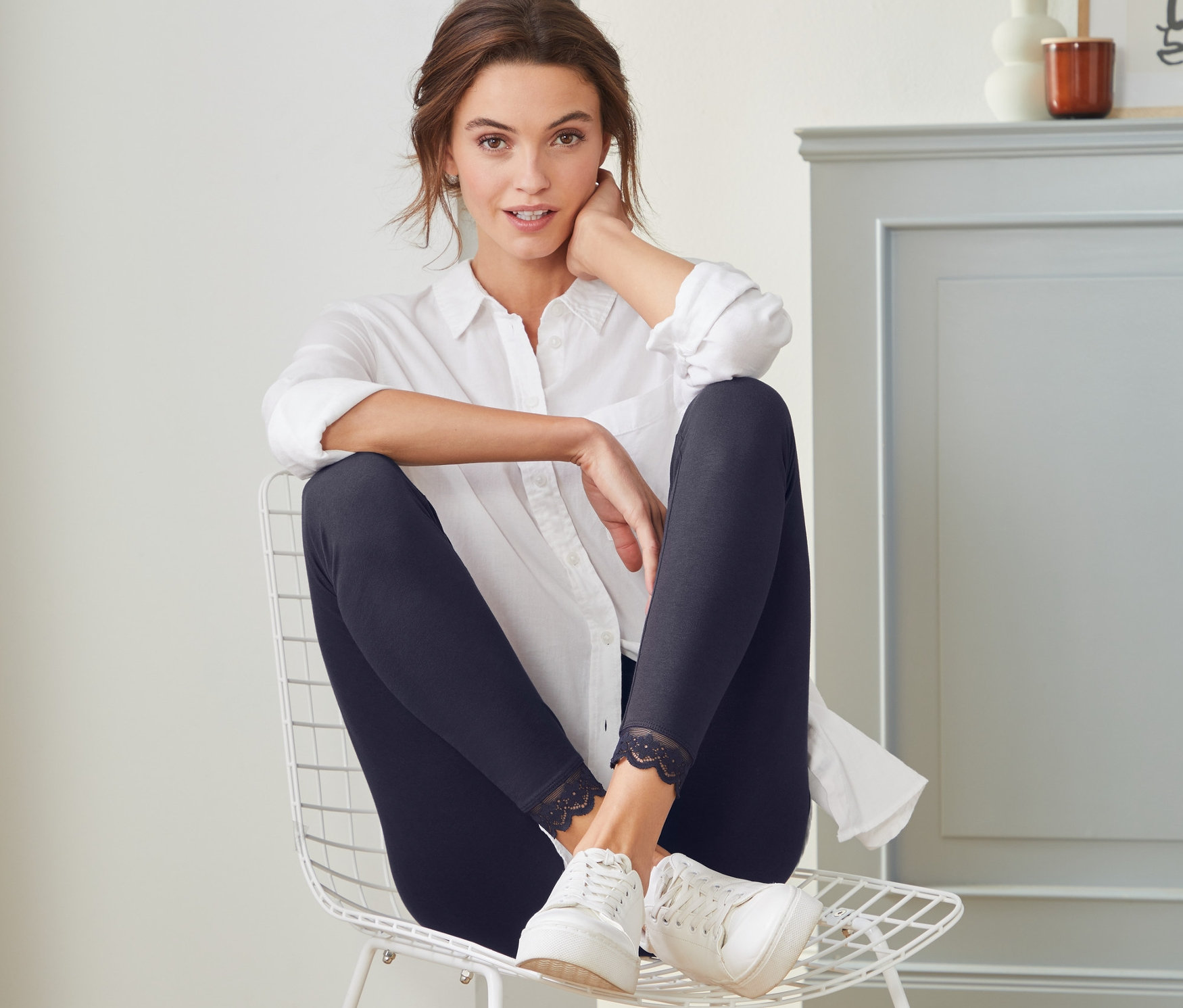 Eine Frau sitzt auf einem Stuhl und trägt Leggings mit Spitzenborte.