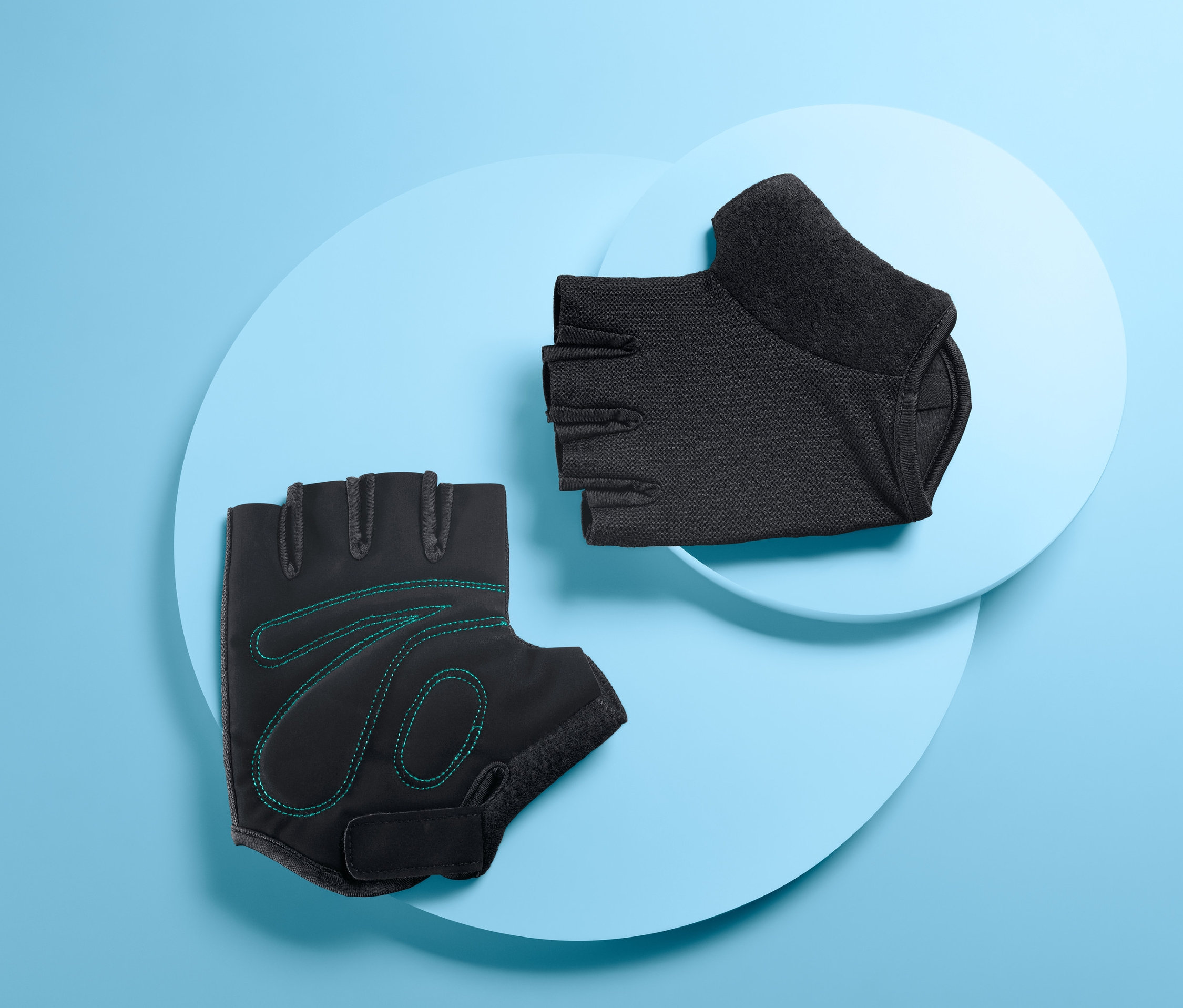 Zwei Fahrrad-Handschuhe liegen übereinander. Ein schwarzer Handschuh hat grüne Ziernähte.