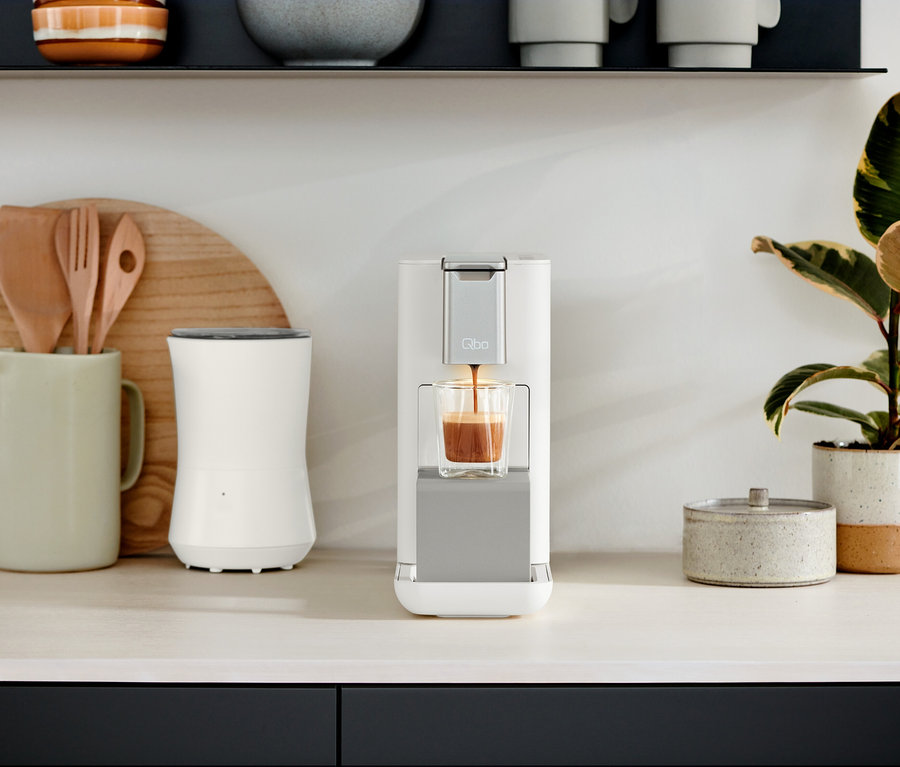 Auf einer Küchentheke stehen Qbo ESSENTIAL Bright Sand und Qbo ICONIC Dark Chrome Kaffeemaschinen.