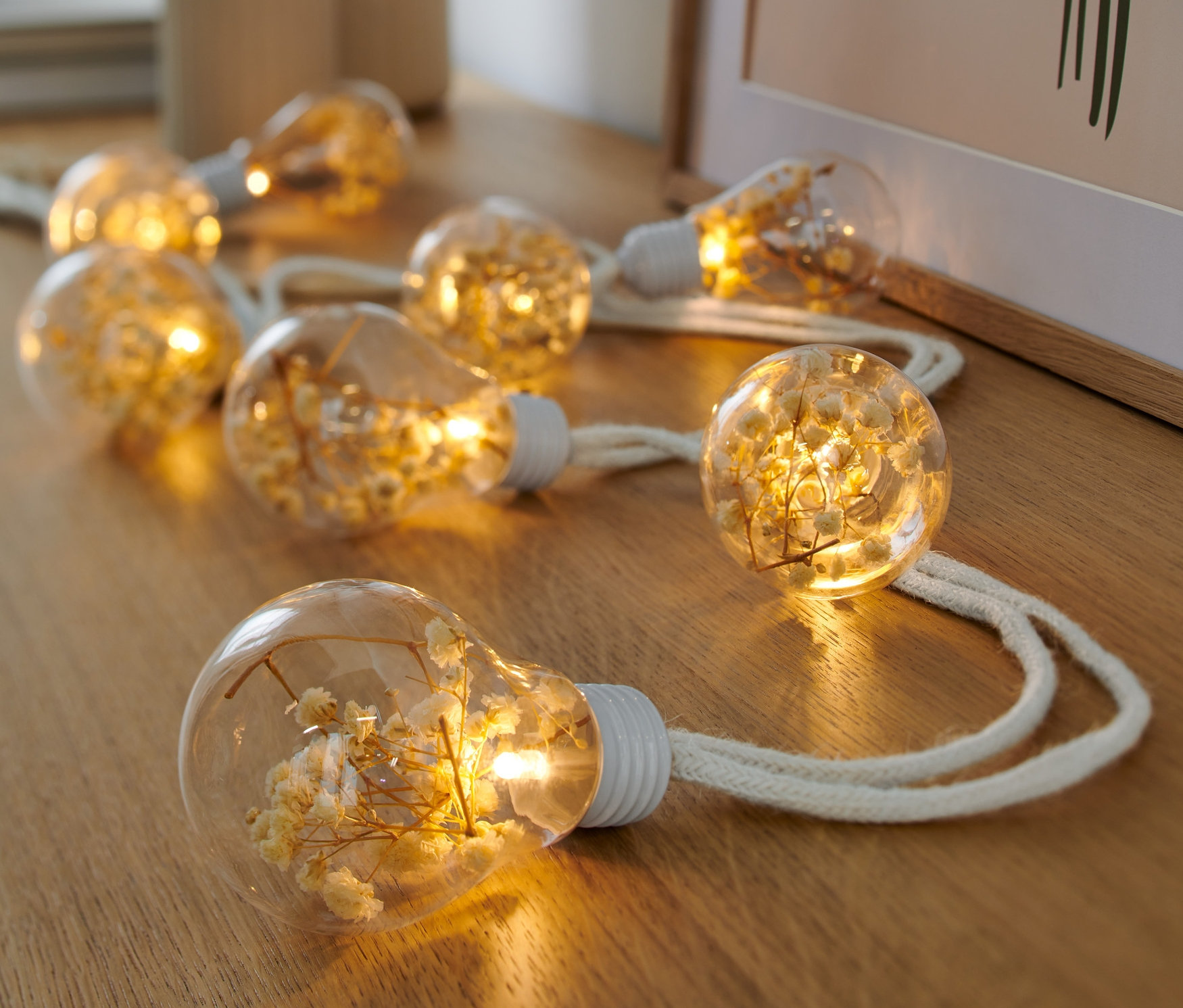 LED-Lichterkette mit Trockenblumen liegt auf einem Holztisch.