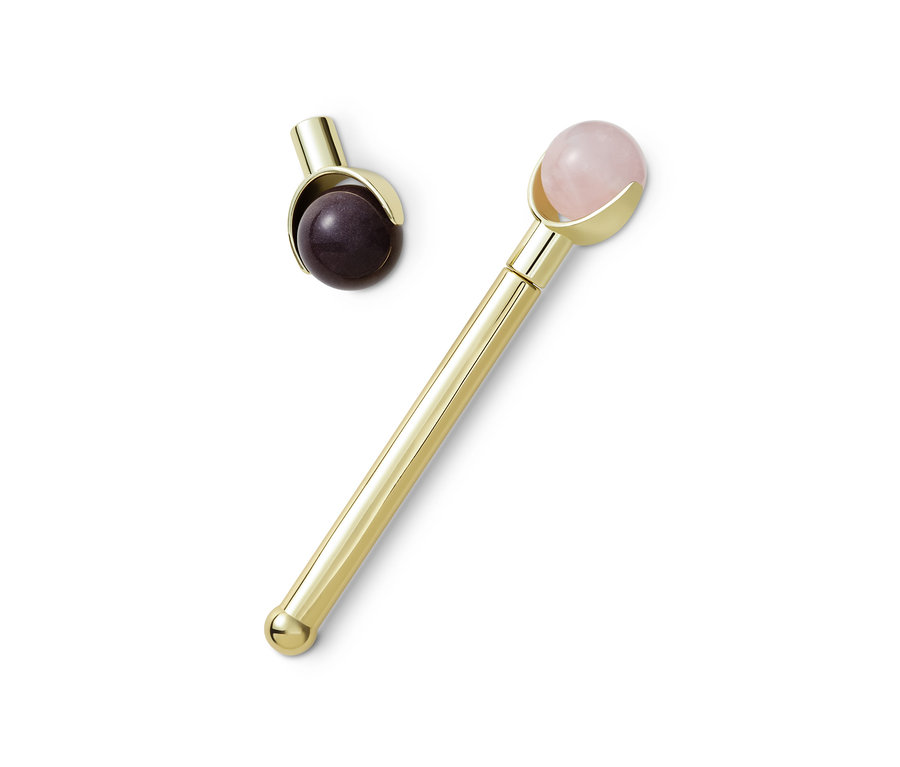 Ein goldener Edelstein-Gesichtsroller und ein kleinerer Gesichtsroller liegen auf einem weißen Hintergrund.