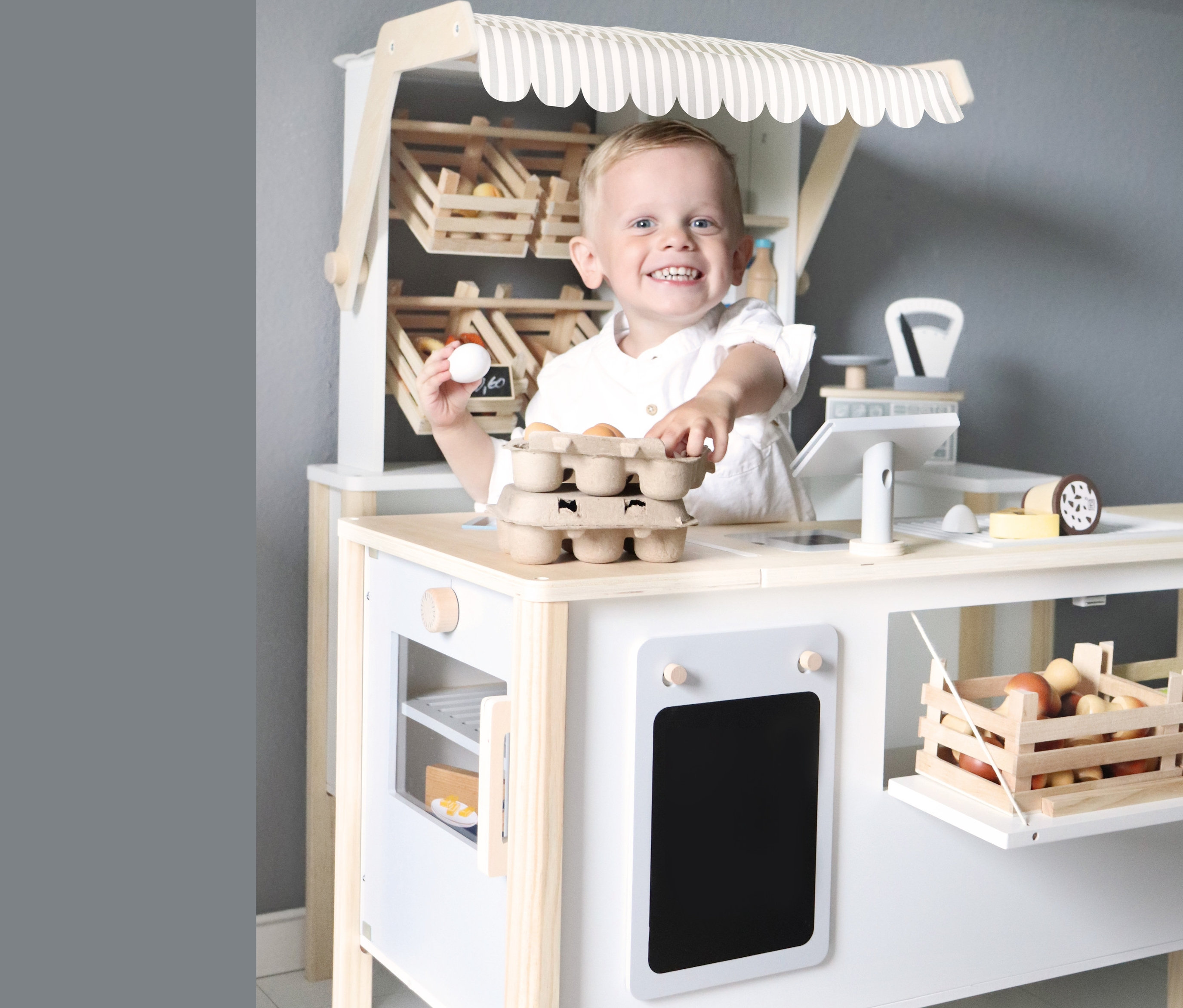 Ein Junge steht an einem small foot Kaufladen und Kinderküche »fresh« und hält ein Ei.