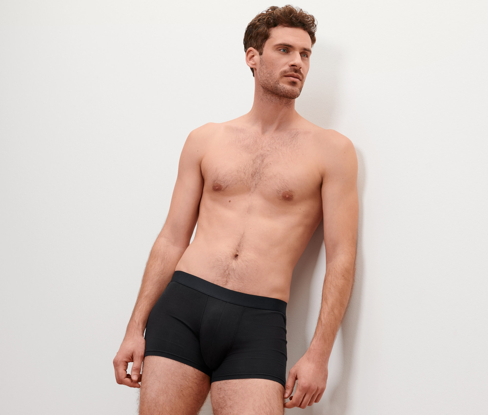 Mann lehnt an einer Wand und trägt 4 Slipboxer in Schwarz.