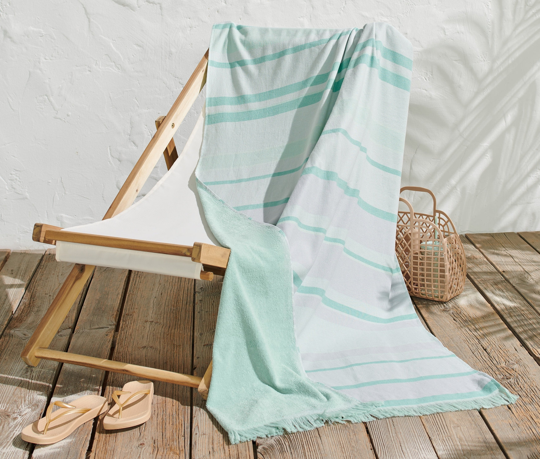Gestreiftes Strandtuch liegt auf einem Liegestuhl neben einem Korb und Zehentrennern.