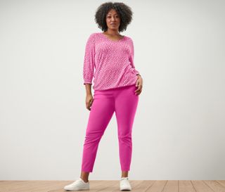 Frau posiert in pinkem, bedrucktem Blusenshirt und pinker Stretchhose.