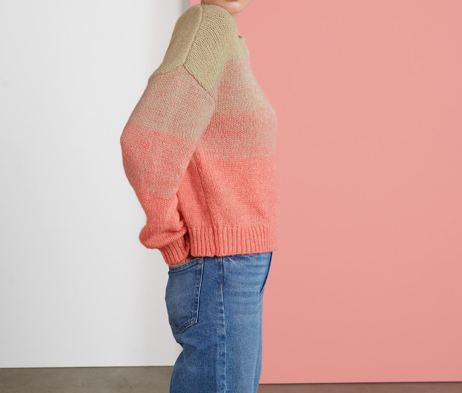 Frau posiert in einem Grobstrick-Pullover und Jeans.