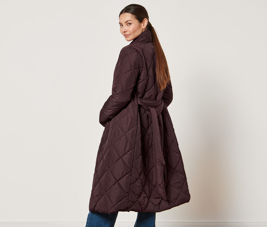 Frau schaut über die Schulter und trägt einen Steppmantel.