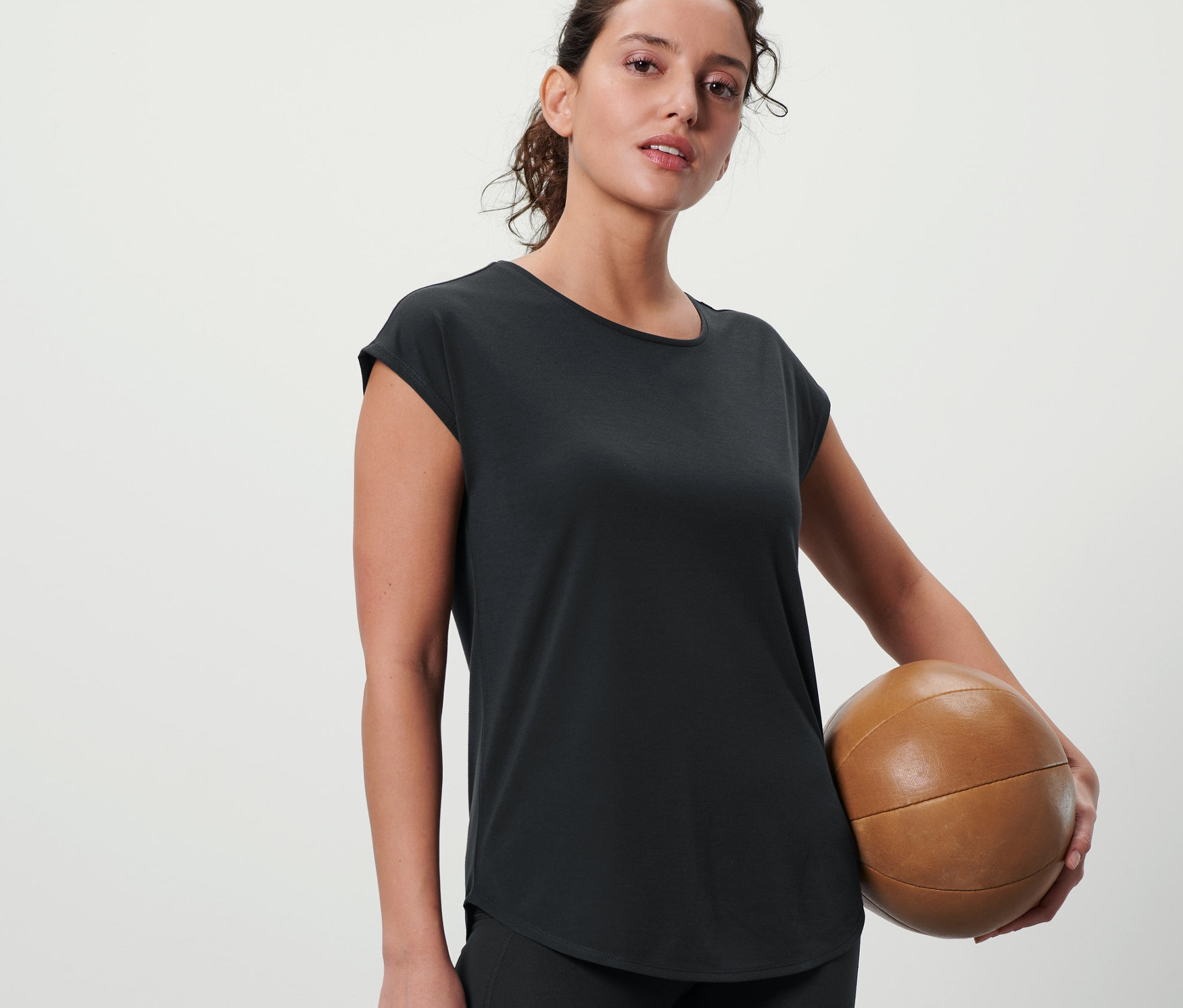 Frau hält Medizinball und trägt ein anthrazitfarbenes Sportshirt.