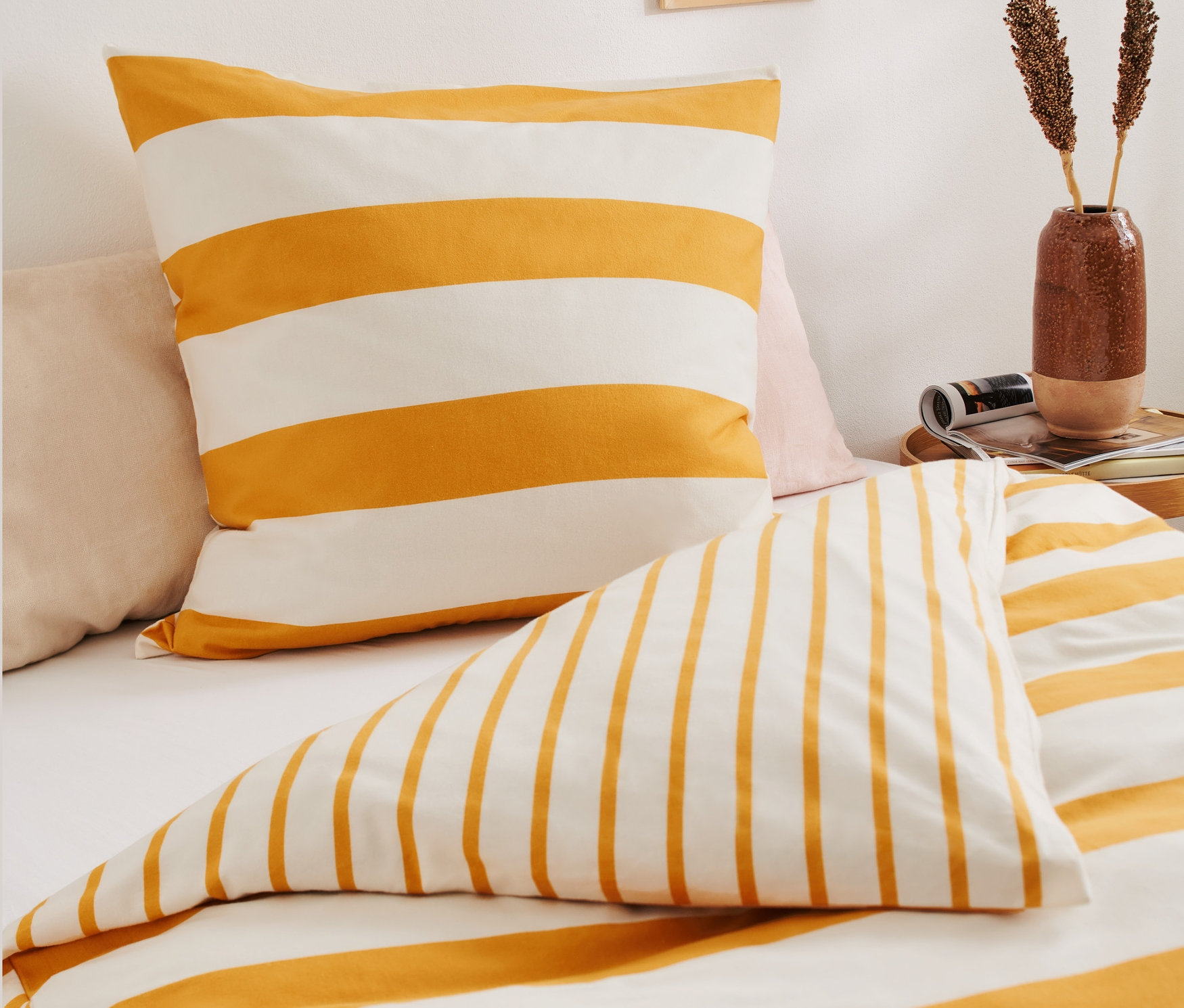 Nahaufnahme eines Bettwäsche-Sets: Kissenbezug und Bettbezug mit gelben und weißen Streifen.