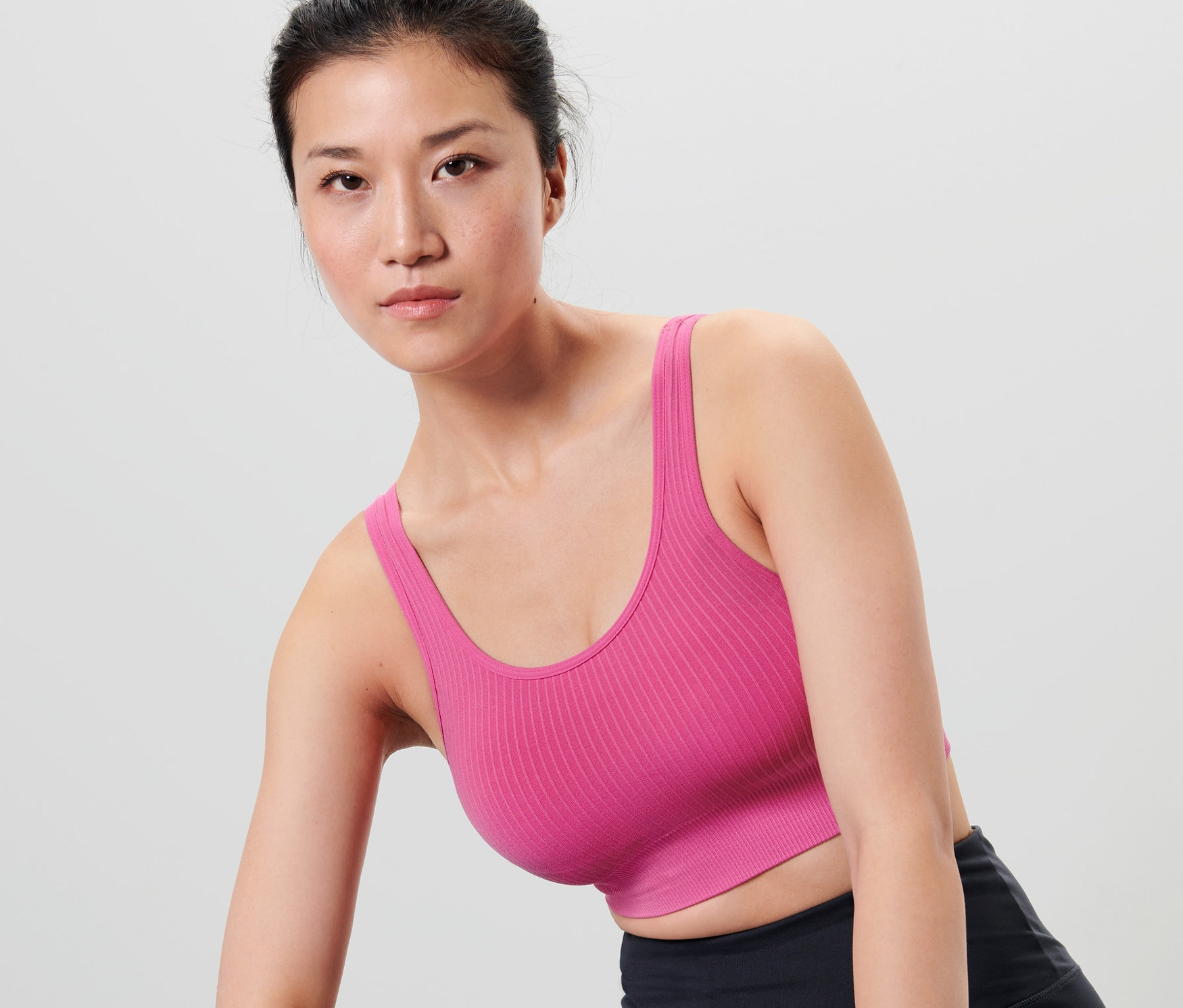 Asiatische Frau trägt ein Seamless-Sport-Bustier, eine schwarze Sport-Shorts und ein lila Schweißband.