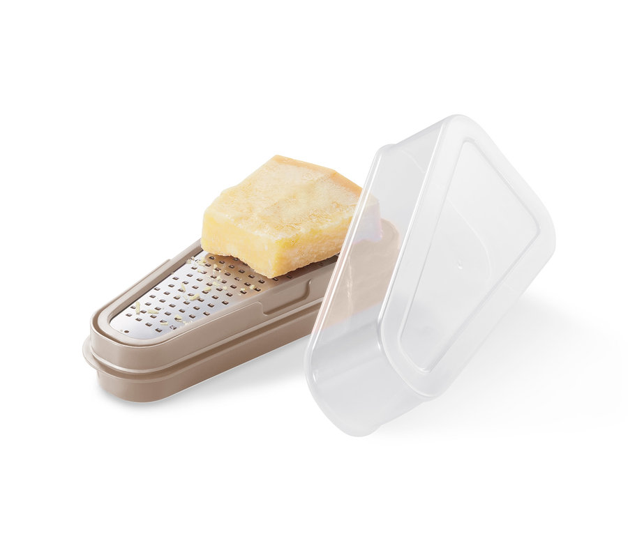 Ein Stück Parmesan liegt auf einer beigen 2-in-1-Parmesanreibe mit transparentem Deckel.
