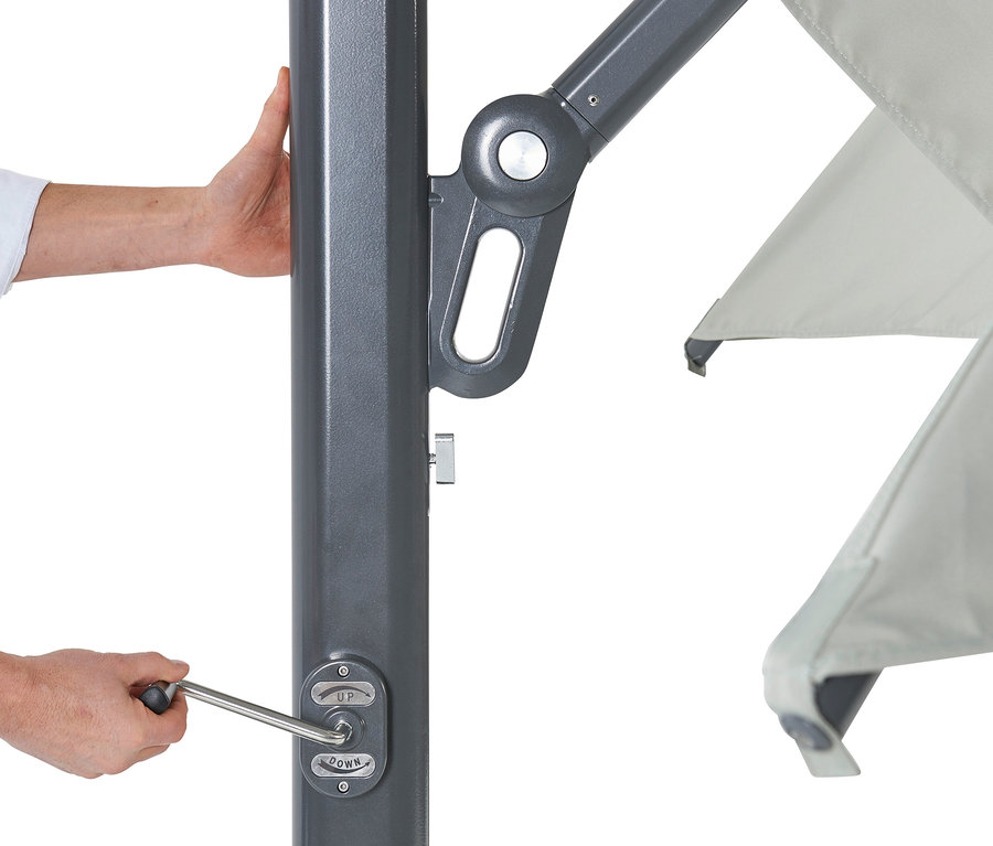 Eine Hand dreht an einer Kurbel an einer grauen Stange, Teilansicht eines hellgrauen Sonnenschirms.