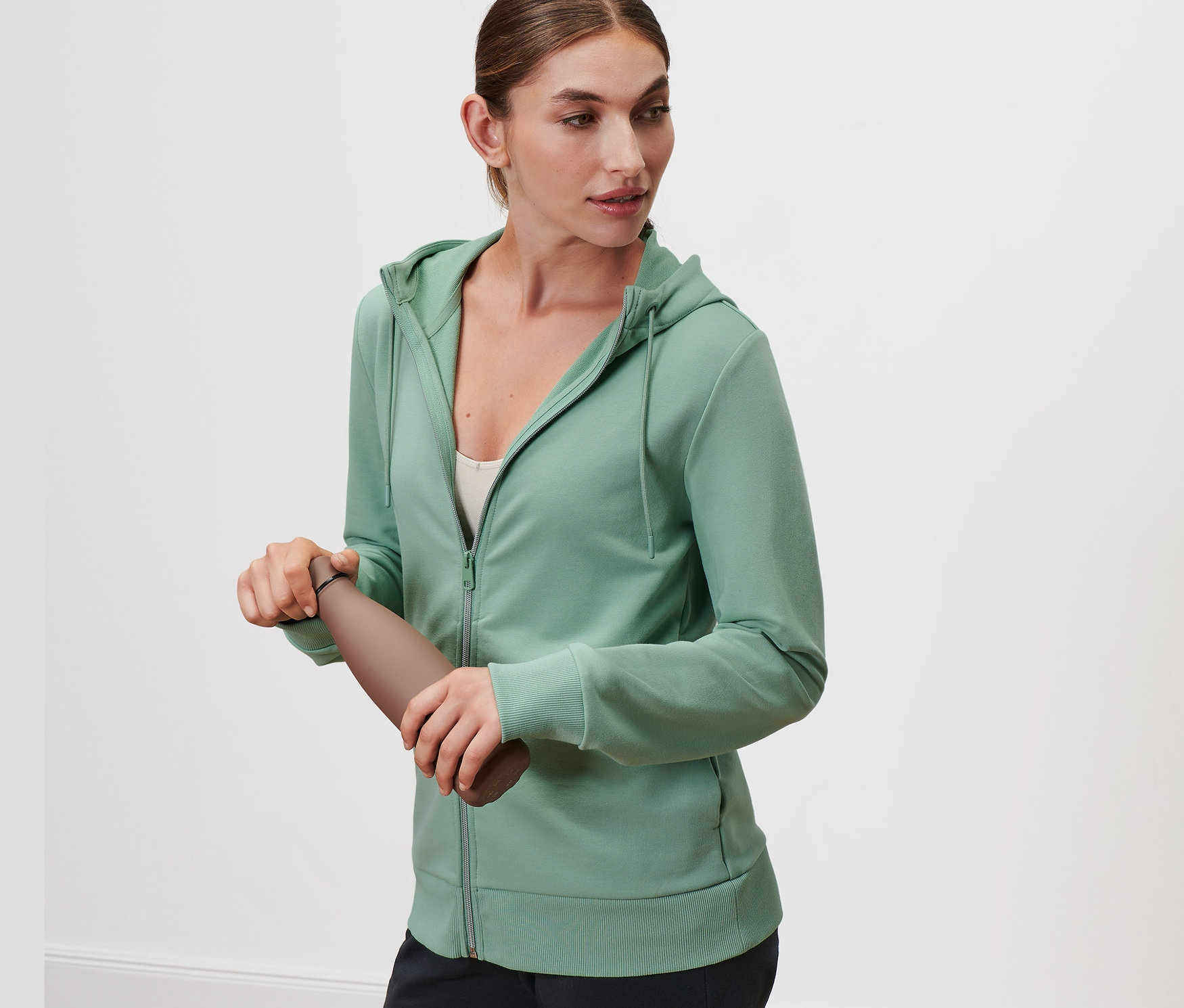 Frau hält eine braune Wasserflasche und trägt eine salbeigrüne Sweatjacke.