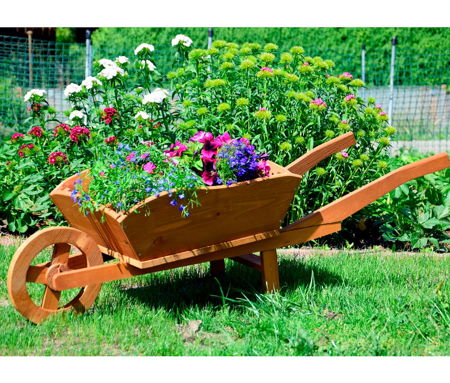 Eine hölzerne Pflanzschubkarre XXL, gefüllt mit Blumen, steht auf einer Wiese.