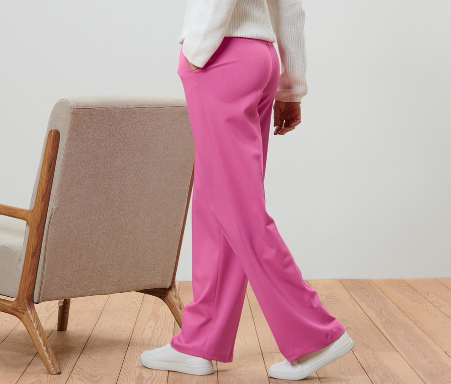 Person geht in pinkfarbener Jerseyhose mit Biese neben einem beigen Sessel.