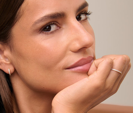 Eine Frau mit braunen Haaren stützt ihr Gesicht auf ihre Hand, sie trägt goldene Creolen und einen 375 Gold Ring Eternity.