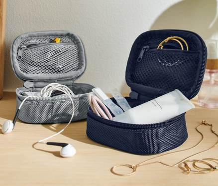 Zwei offene Mini-Reise-Ordnungstaschen, eine graue mit weißen Kopfhörern und eine marineblaue mit Kosmetika und Goldschmuck.
