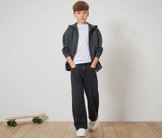 Junge steht mit Händen in den Taschen in Kinder-Jeans ‒ Fit »Finn« und Zip-Hoodie.