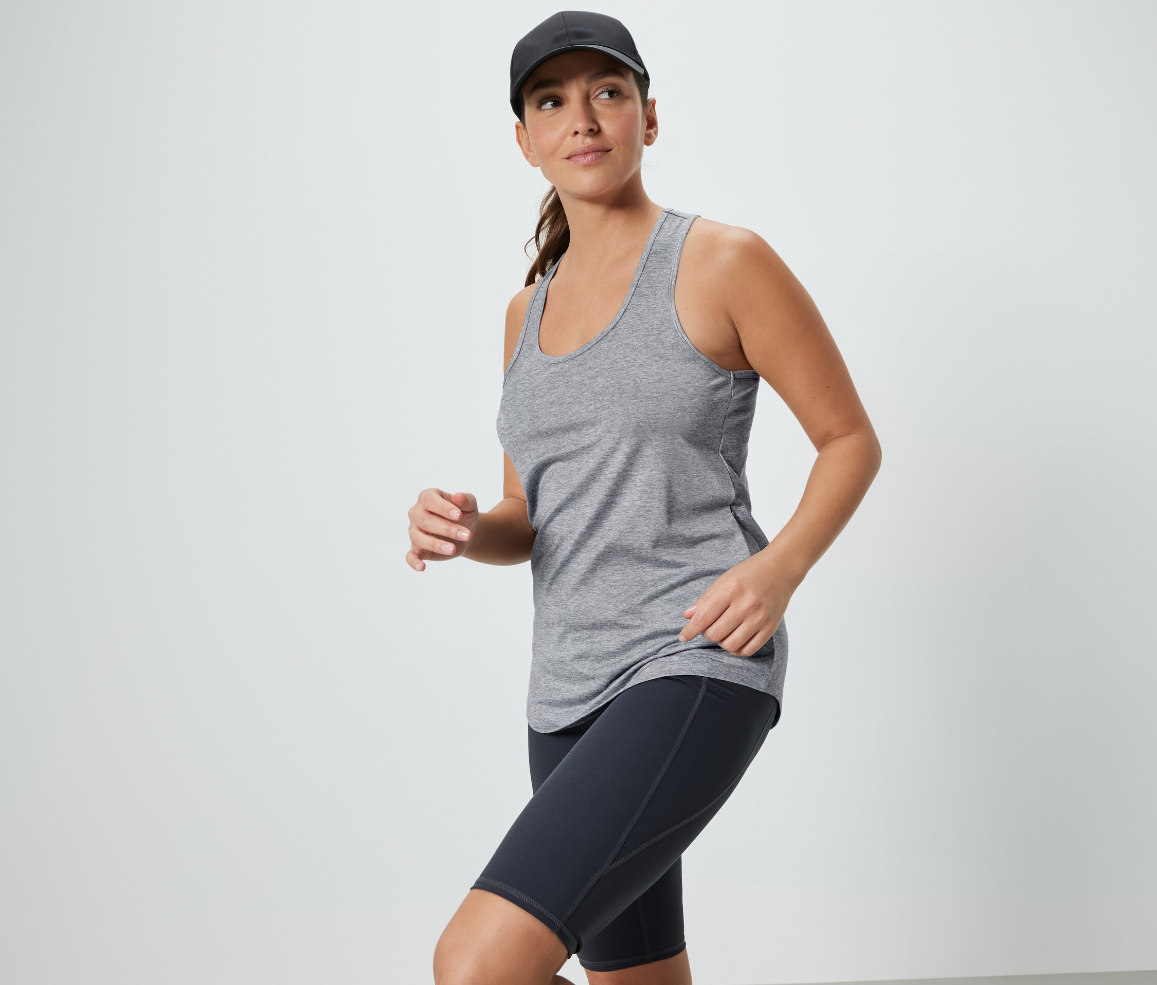 Frau trägt graues Top und schwarze Radlerhose mit Kappe. 2 Funktionstops, schwarz und grau.