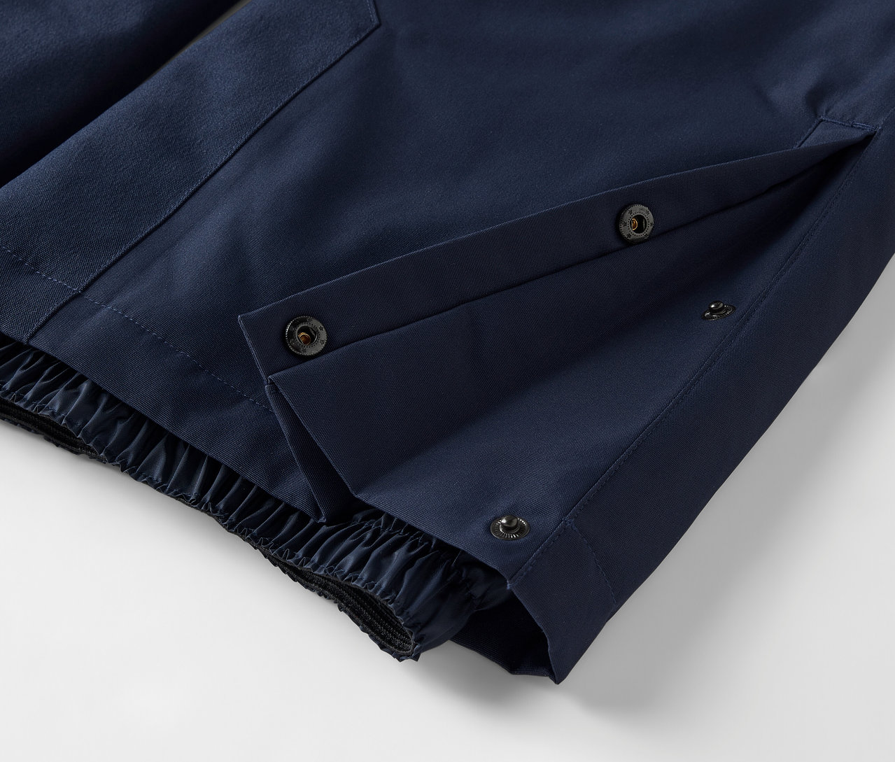 Detail einer blauen Hose mit Druckknopfverschluss und elastischem Saum.