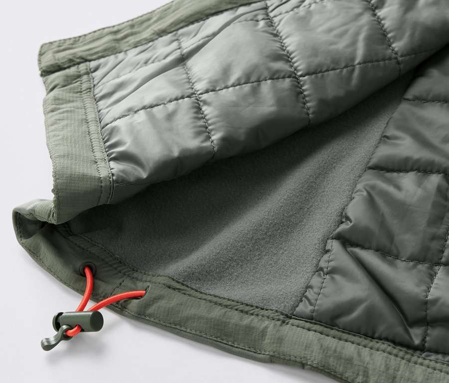 Detail einer olivgrünen Steppweste »pack light« mit orangefarbener Zugschnur.