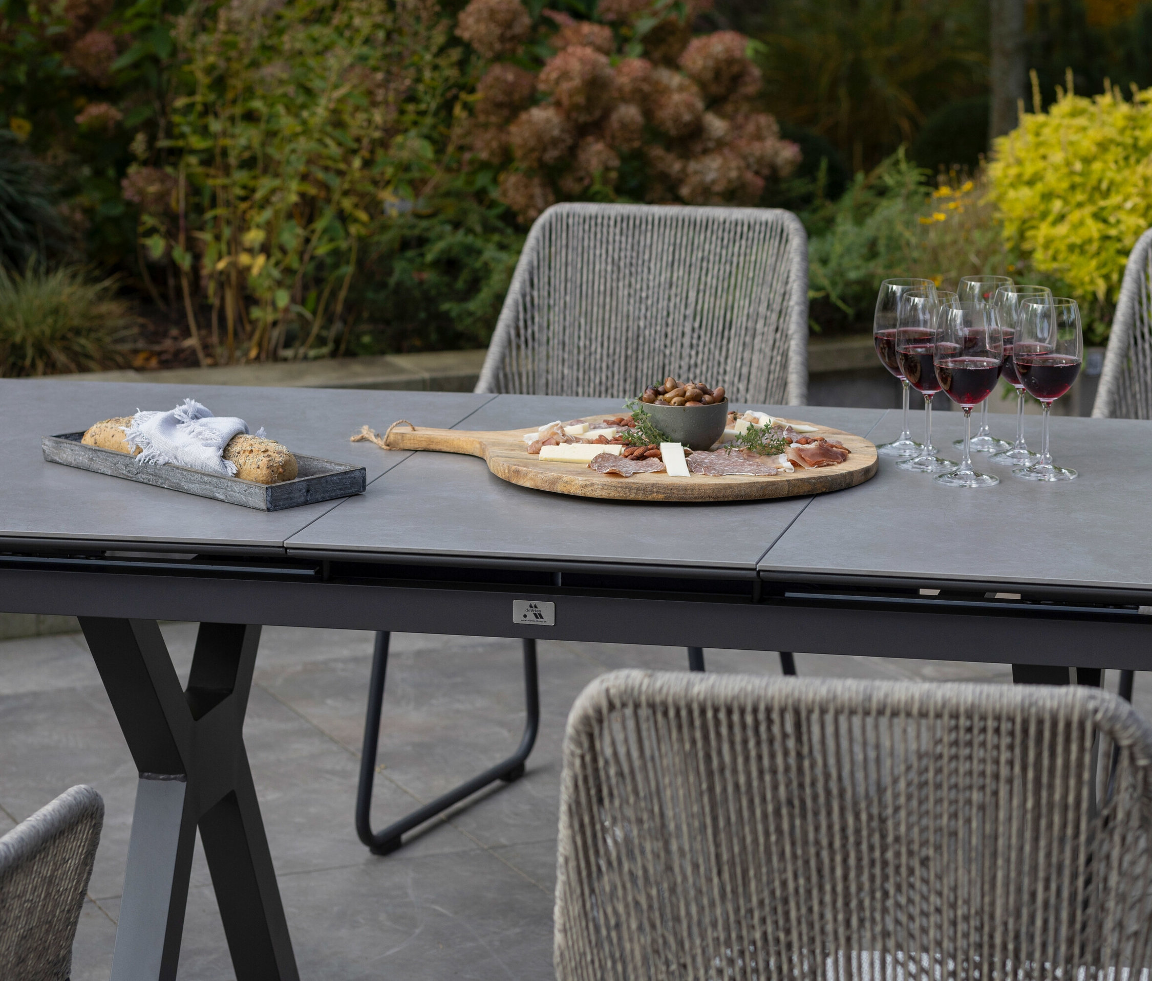 Auf einem hellgrauen deVries Ausziehtisch 160/210 stehen Brot, ein Brett mit Speisen und Weingläser.