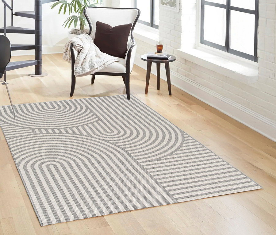 Ein grau-weißer Outdoor-Teppich »Arc Symphony« mit geometrischem Muster liegt in einem Wohnzimmer.