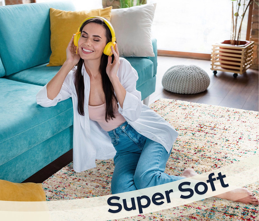 Frau sitzt auf »Relic« Teppich in gedämpften Pastellfarben und hört Musik mit gelben Kopfhörern.