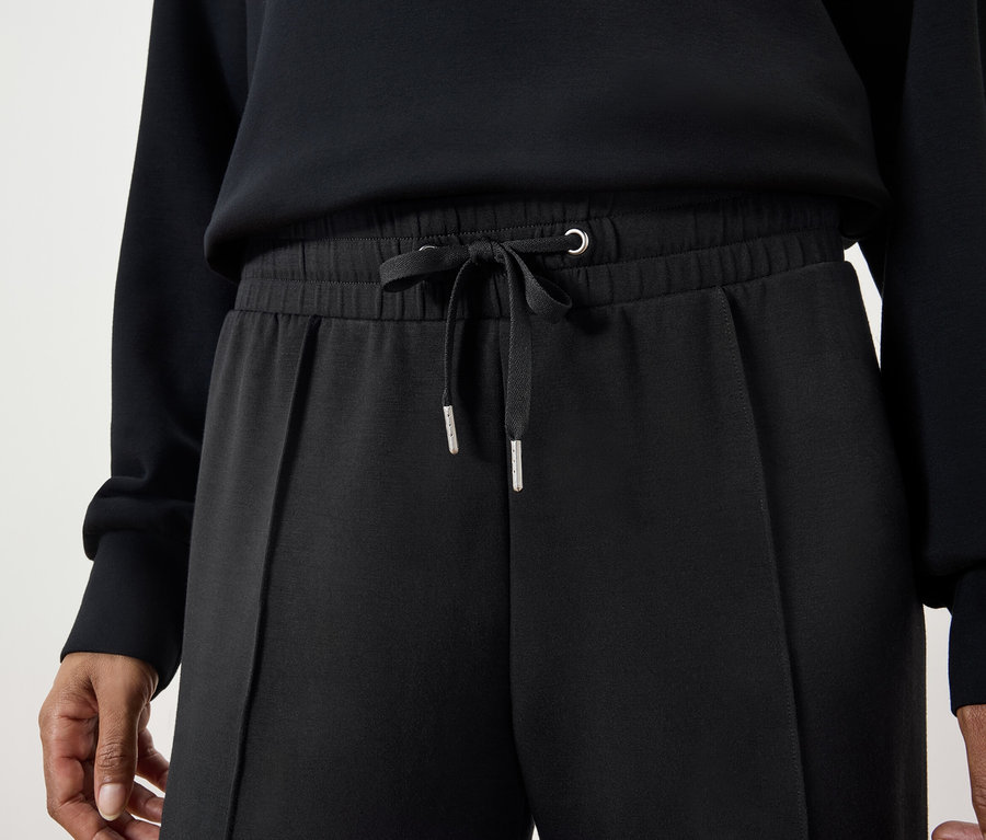 Detailaufnahme einer Frau, die eine schwarze Hose mit Kordelzug und einen schwarzen Pullover trägt.