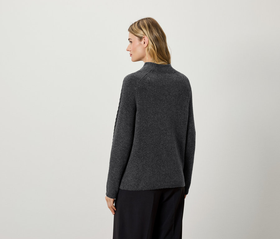 Frau mit dem Rücken zur Kamera trägt einen dunkelgrauen Pullover und eine schwarze Hose.