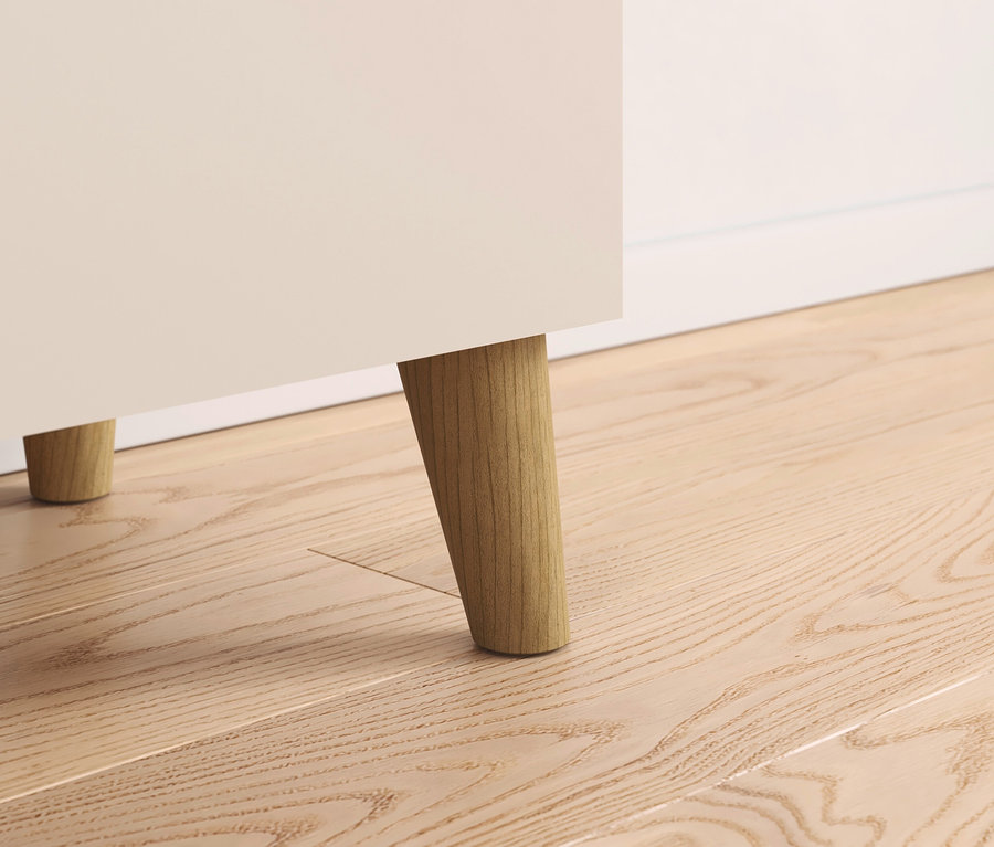 Detailaufnahme eines cremefarbenen Schranks mit Holzfüßen auf einem Holzboden.