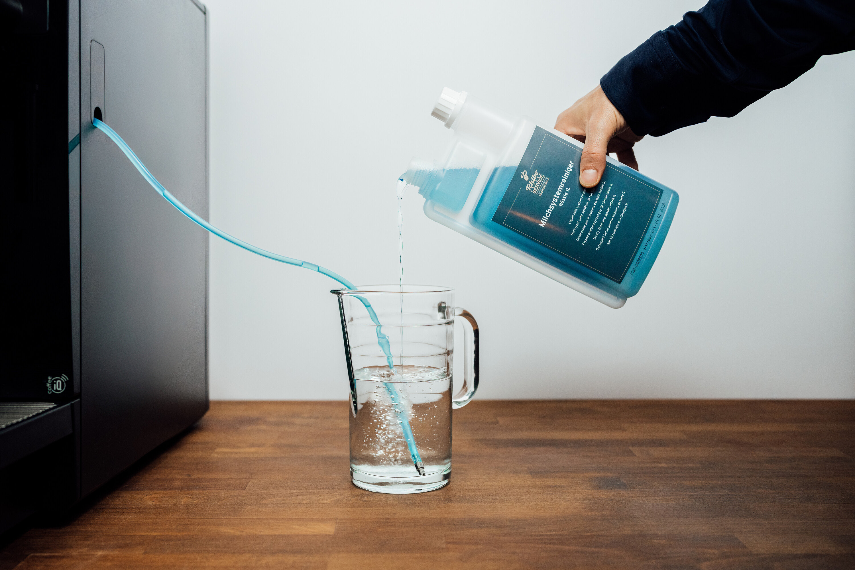 Person gießt flüssigen Reiniger in ein Glas, ein Schlauch führt zum Kaffeevollautomaten.