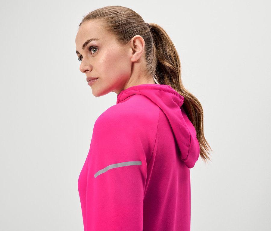 Frau mit braunen Haaren, die zu einem Pferdeschwanz zusammengebunden sind, trägt einen pinkfarbenen Kapuzenpullover.