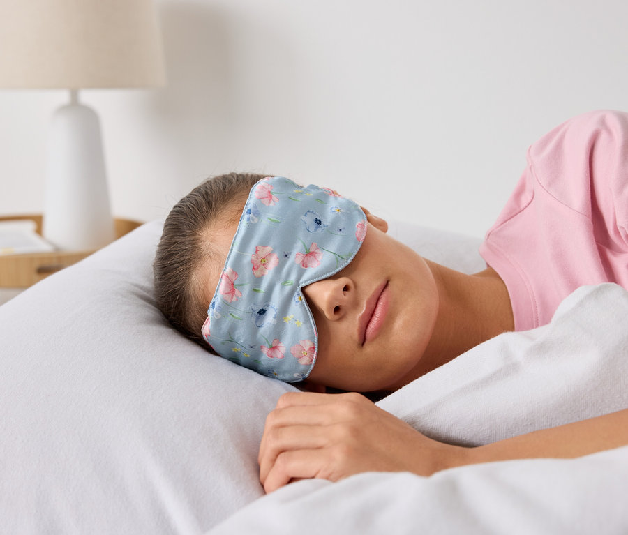 Frau schläft mit einer Schlafmaske mit Blumenmuster im Bett.