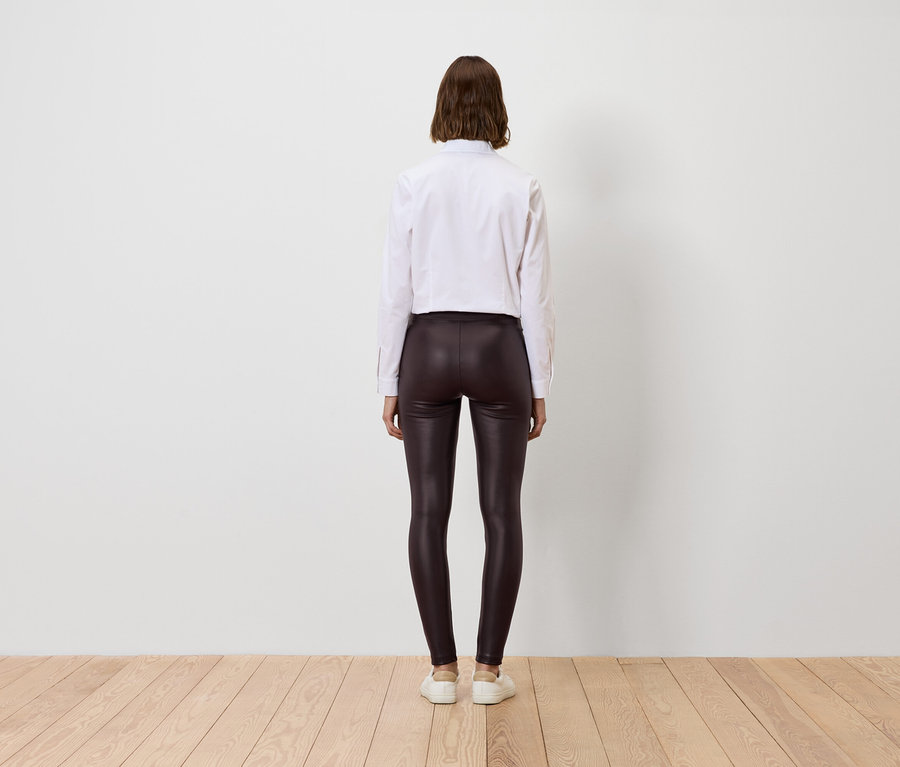 Frau von hinten in weißem Hemd und glänzenden braunen Leggings.