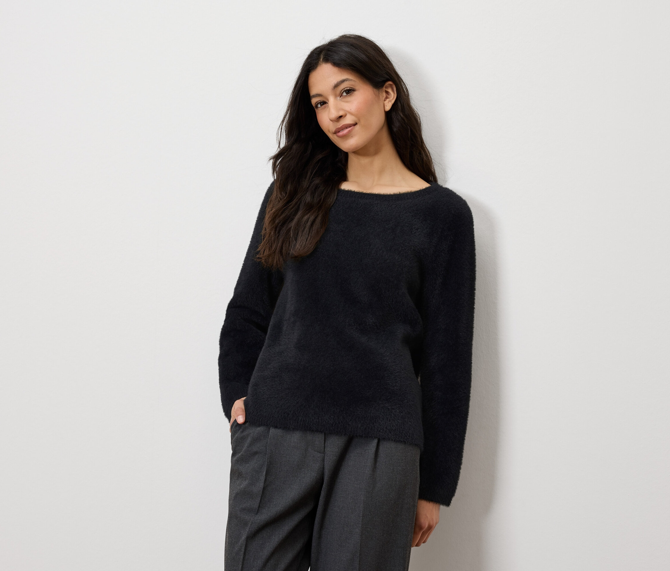 Frau posiert in marineblauem Pullover und grauer Hose.