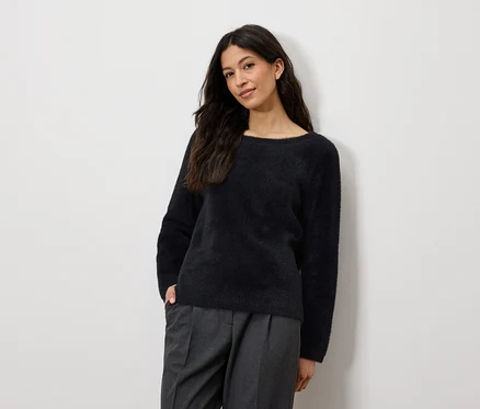 Frau posiert in marineblauem Pullover und grauer Hose.