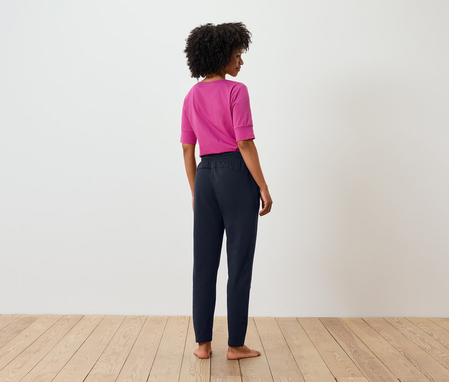 Rückansicht einer Frau mit Afro, die ein pinkes T-Shirt und eine marineblaue Hose trägt.