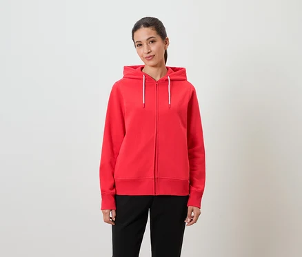 Eine Frau trägt einen roten Kapuzenpullover und eine schwarze Hose.