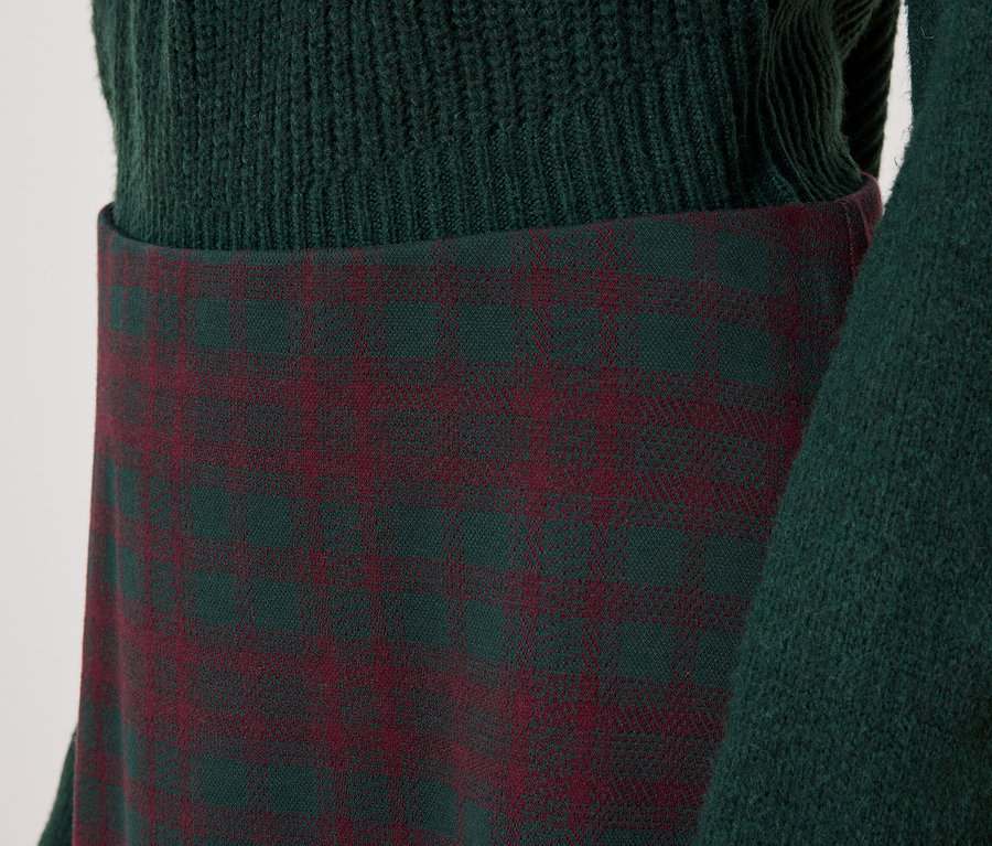 Detail eines Damenoutfits mit grünem Pullover und kariertem Rock.