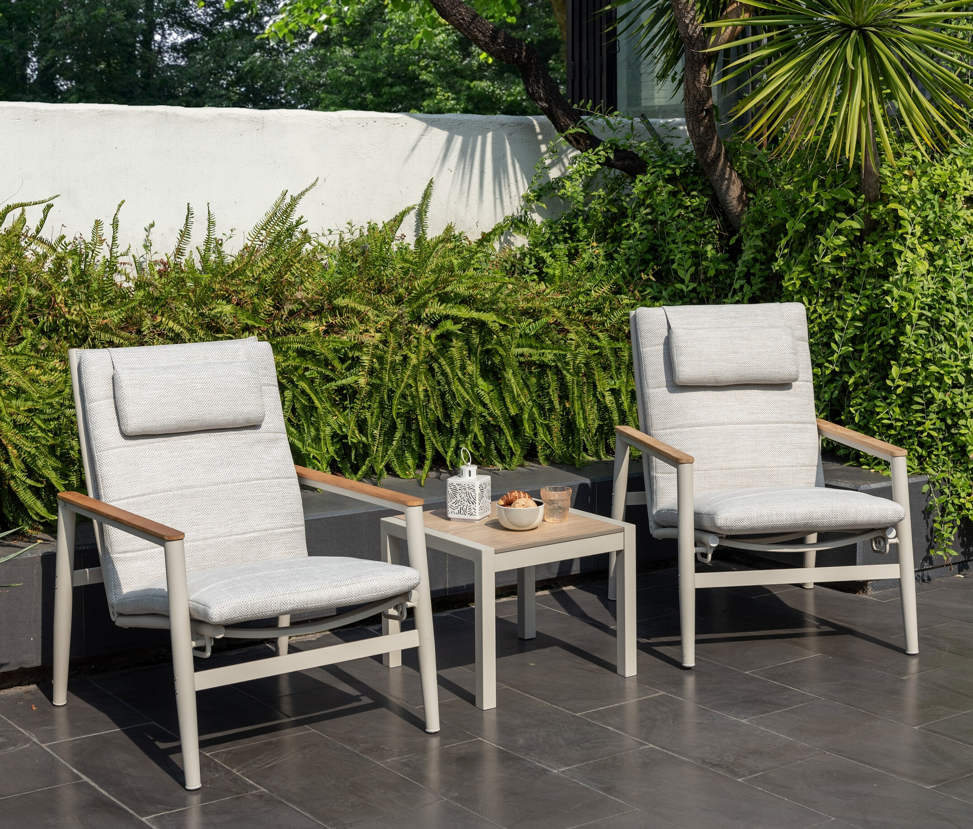 Zwei hellgraue ScanCom Outdoor-Loungesessel mit verstellbarer Rückenlehne und ein Tisch mit Erfrischungen auf einer Terrasse.