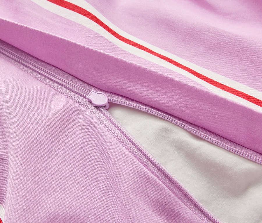 Nahaufnahme eines teilweise geöffneten, lila Bettbezugs mit rot-weißen Streifen und einem Reißverschluss, der einen Blick auf das weiße Innere freigibt.