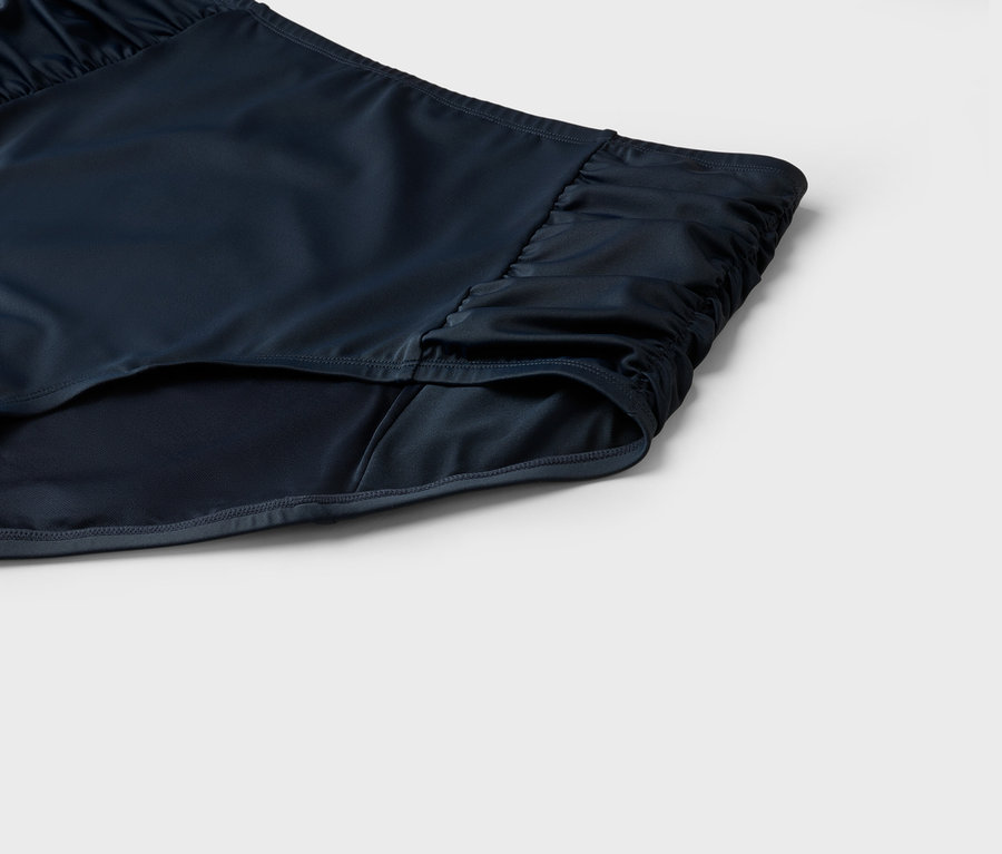 Nahaufnahme einer dunkelblauen Badehose mit Raffung an der Seite vor einem neutralen Hintergrund.