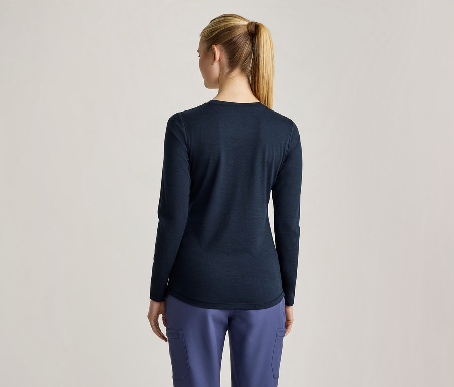 Eine Frau von hinten gesehen, die ein dunkelblaues Langarmshirt und hellblaue Cargohosen trägt. Ihr blondes Haar ist zu einem Pferdeschwanz gebunden.