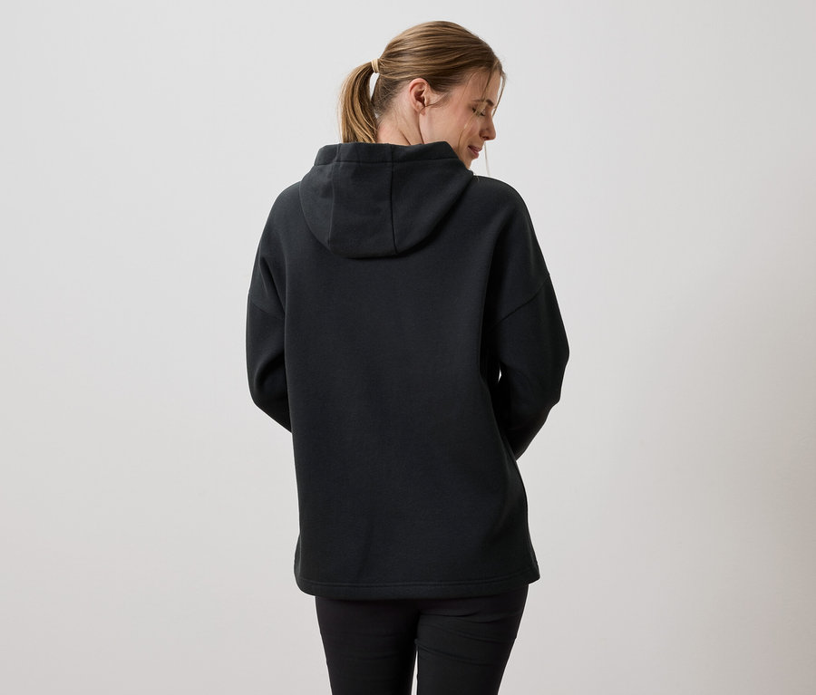 Rückansicht einer Frau mit blonden Haaren, die einen schwarzen Kapuzenpullover und schwarze Leggings trägt.